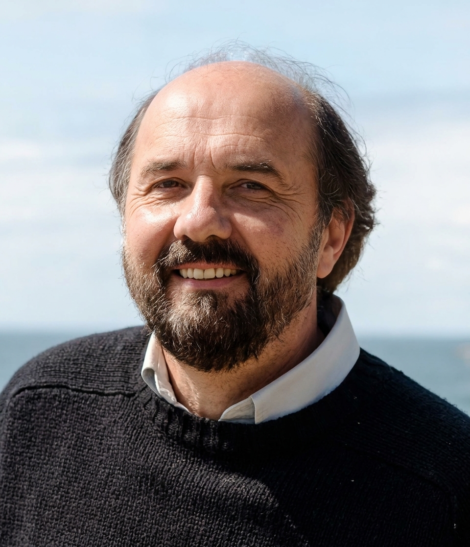 Portrait of author Lew Osteen — a bearded man smiling with the sea and sky behind him